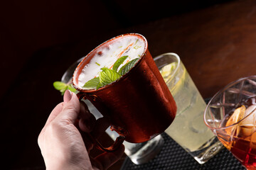 holding a moscow mule cocktail in snake mug with blurred drinks in the background