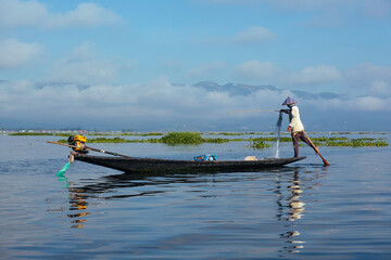 Myanmar, lac Inle - pêcheur Birman en équilibre sur sa pirogue, une jambe manoeuvre la rame pour...