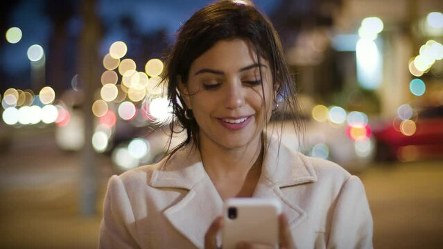 
Lateral Dolly of Attractive and Cheerful Young Woman Using Smartphone in Crowded Street. Texting on Mobile Phone at Night with Traffic.