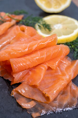 Slices of tasty smoked Scottish salmon fish served on black plate with lemon and fresh dill