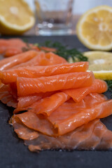 Slices of tasty smoked Scottish salmon fish served on black plate with lemon and fresh dill