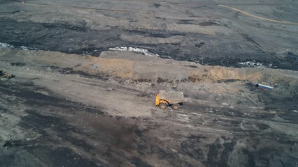 Grader lays new road in quarry next to overweight dump truck carrying coal. Aerial view