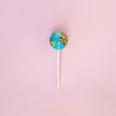 Globe lollipop on pastel light pink background. Minimalistic environment composition. Creative candy world flat lay. Beauty of the planet idea. World Earth day concept.