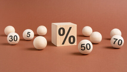percent sign on wooden cubes against broun background with wooden balls. concept of sale and...