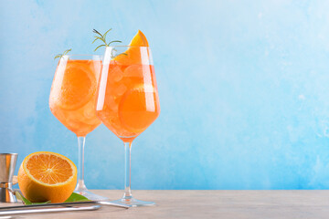 Classic italian aperitif aperol spritz cocktail in two wineglasses with ice cubes and slice of orange with light blue background on beige stone background, traditional summer fresh iced drink, closeup