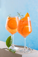 Classic italian aperitif aperol spritz cocktail in two wineglasses with ice cubes and slice of orange with light blue background on marble stone podium, traditional summer fresh iced drink, close up