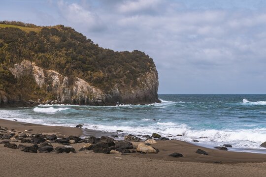 Beautiful landscape of a sandy beach by a rocky cliff in Praia de Moinhos