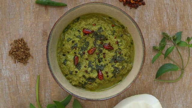 Mint and coconut chutney (Pudina chutney) in bowl with main ingredients: mint, coconut, roasted chana dal, cumin and green chilies. Top view, table spin.