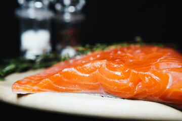 Fresh raw salmon fillet with seasonings and herbs, close-up on black background.