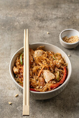 Asian funchose salad with chicken and vegetables in bowl with wooden chopsticks on textured green background with text space. Food menu