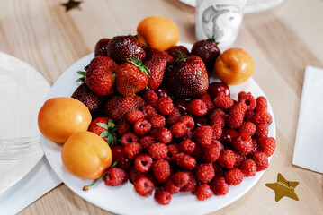 a lot of beautiful juicy raspberries, strawberries and peaches on a white plate
