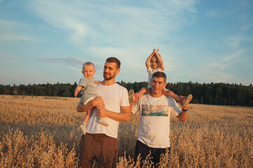 two fathers with two children walk at sunset in an oat field.