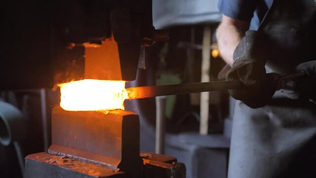 A blacksmith hammers hot iron with a mechanical hammer