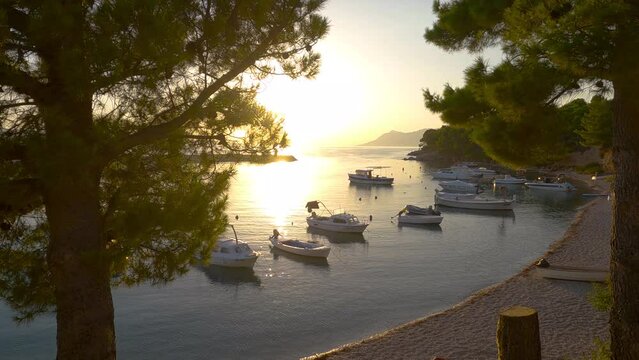 Beautiful sunset on the beach with boats in the small Croatian harbor of Makarska Riviera in slow motion, 4k.