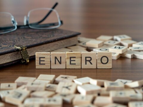 enero palabra o concepto representado por baldosas de letras de madera sobre una mesa de madera con gafas y un libro
