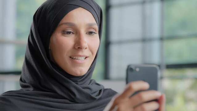 Close-up positive arab woman in hijab holding phone making order in online store friendly smiling muslim female consultant responding to client in web chat using smartphone chatting with friend remote