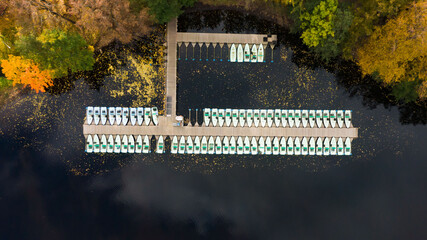 Aerial view of the wooden pier with pleasure boats on the lake in the autumn city park