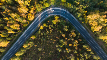 Aerial view of a bend in the road with cars in the middle of yellow autumn trees