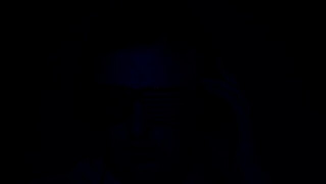 A young stylish man at the event listens musically with a smile to the music in the earphone and dances. Young DJ in headphones plays music in a night club in neon color
