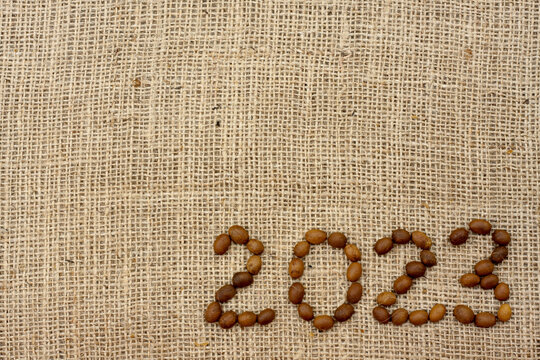 numbers 2023 are made from coffee beans on fabric with burlap texture. View from above. Place for text. Background for design.