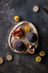 Autumn fruits, black fig and yellow plums on wooden tray. Flat lay, top view on dark textured background with dry poppy plants and hemp cord. Fruits in Fall season.