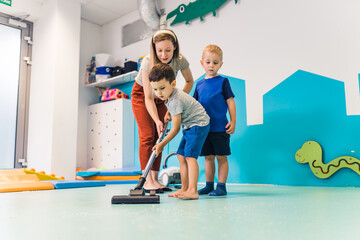 Little helpers, toddlers boys vacuuming, helping their teacher to clean the room after play at the...