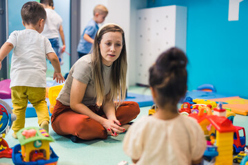 Nursery school. Toddlers and their tutor playing with colorful plastic playhouse, cars and boats. Imagination, mathematical ability, fine motor and gross motor skills development. High quality photo
