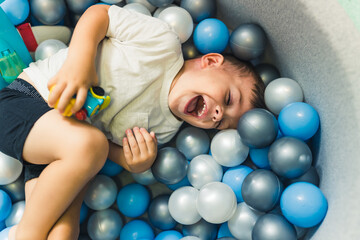 Happy toddler boy playing in a ball pit full of colorful balls. Sensory play at the nursery school...