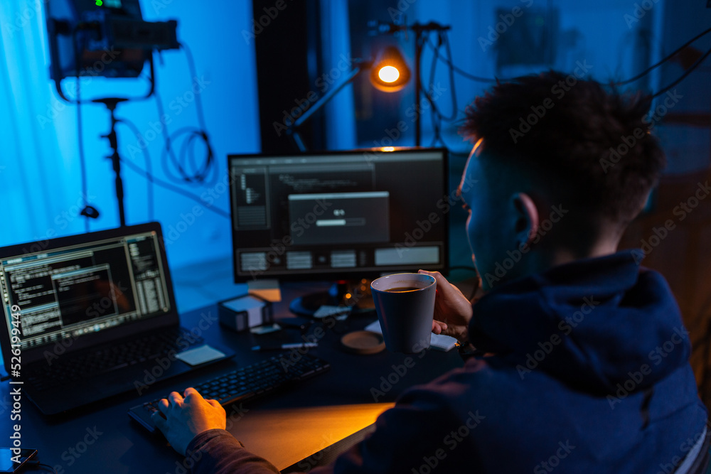 Poster cybercrime, hacking and technology concept - male hacker in dark room drinking coffee and using comp
