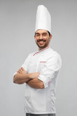 cooking, culinary and people concept - happy smiling male chef in toque and jacket with crossed...