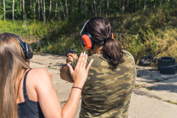 Unrecognizable long-haired caucasian female showing instructor correcting the posture of a black-haired man in moro t-shirt holding a gun. Outdoor shot. High quality photo