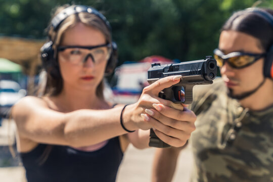 A day in a shooting range. Confident caucasian young adult girl aiming at target with a black gun. Protective eyeglasses and headphones. Private shooting lesson. High quality photo