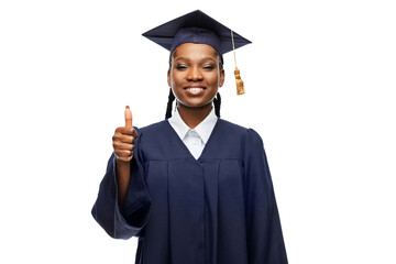 education, graduation and people concept - happy graduate student woman in mortarboard and bachelor gown showing thumbs up