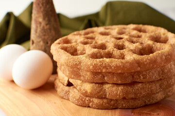 Fritters placed on a wooden base and around a panela and two eggs.