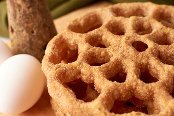 Fritters placed on a wooden base and around a panela and two eggs.