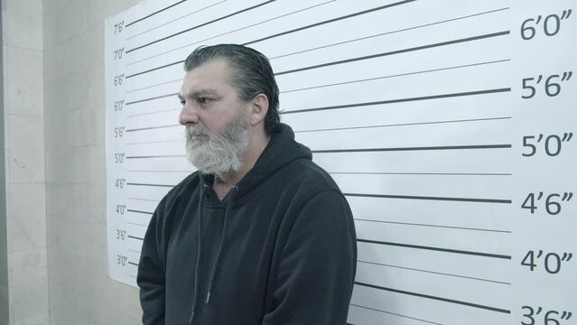 Portrait of the arrested male caucasian mature prisoner during mug shot scene in a police station. Crane shot, slow-motion.