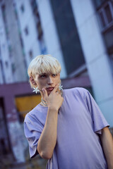 A teenager is posing outside surrounded by buildings on the street.