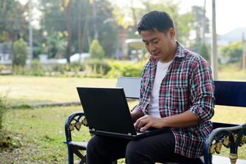  Asian man works on computer laptop at the park. Concept : remote working through technology internet. Everywhere we can work.                       