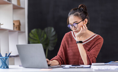 Portrait of Business Asian woman sitting at at laptop and thinking of problem solution, working schedule for employee writing report into notebook while using laptop computer in coworking space