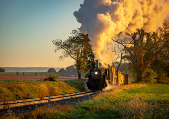 A View of an Antique Freight Steam Train Blowing Smoke Approaching Thru Trees in Late Afternoon