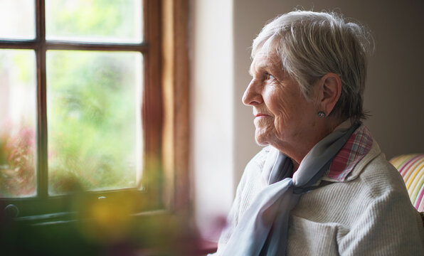 Happy elderly woman looking out window thinking of memories pensioner retirement lifestyle concept