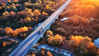 The truck is driving across the bridge over the river Drone view of the autumn forest.