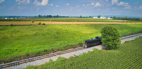 A Drone View of a Single Lonely Diesel Engine Traveling Along a Single Railroad Track, Through Farmlands on a Sunny Day