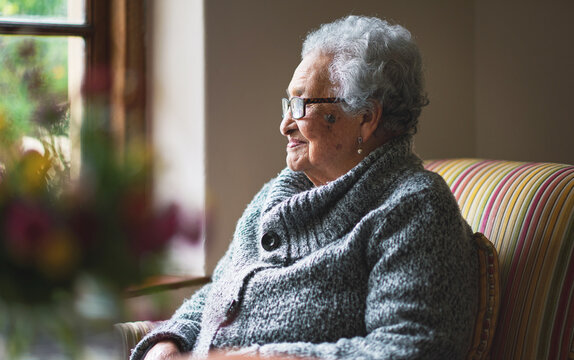 Happy elderly woman looking out window thinking of memories pensioner retirement lifestyle concept