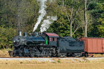 Fototapeta na wymiar A View of a Steam Freight Train on a Single Track Going Thru Rural Countryside on a Sunny Day