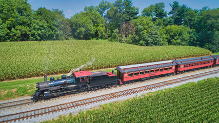 Drone View of an Antique Steam Engine, Approaching, Blowing Steam and Traveling Along the Countryside on a Sunny Day