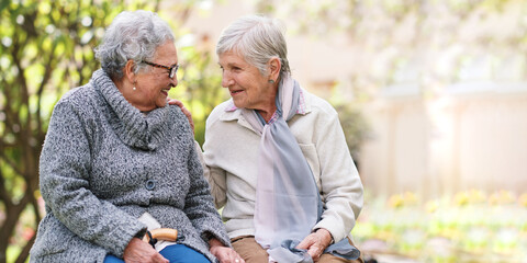 Two elderly women sitting on bench in park smiling happy life long friends enjoying retirement