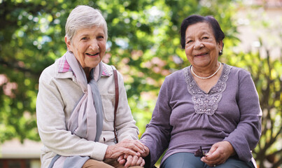 Two elderly women sitting on bench in park holding hands smiling happy life long friends enjoying...
