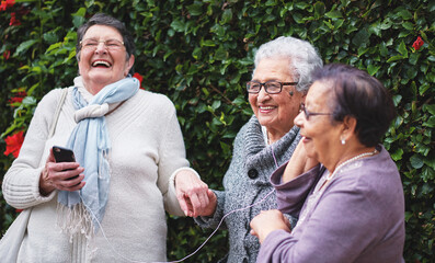 Funny elderly women listening to music on smartphone wearing earphones smiling enjoying fun...