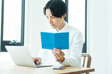 年金手帳とパソコンを見る日本人男性 - obrazy, fototapety, plakaty